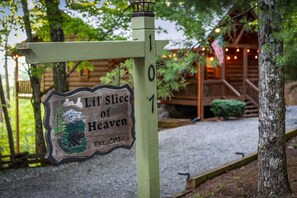 A wooden sign with a bear and mountain, a cabin, and a porch with lights. - Lil' Slice of Heaven- Pet Friendly | Hot Tub | Fire Pit | Cherry Log (Cherry Log)