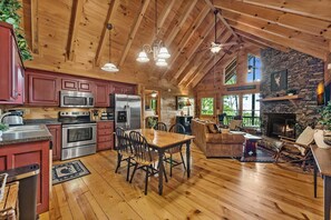 A spacious cabin interior with a kitchen, dining area, and stone fireplace. - Lil' Slice of Heaven- Pet Friendly | Hot Tub | Fire Pit | Cherry Log (Cherry Log)
