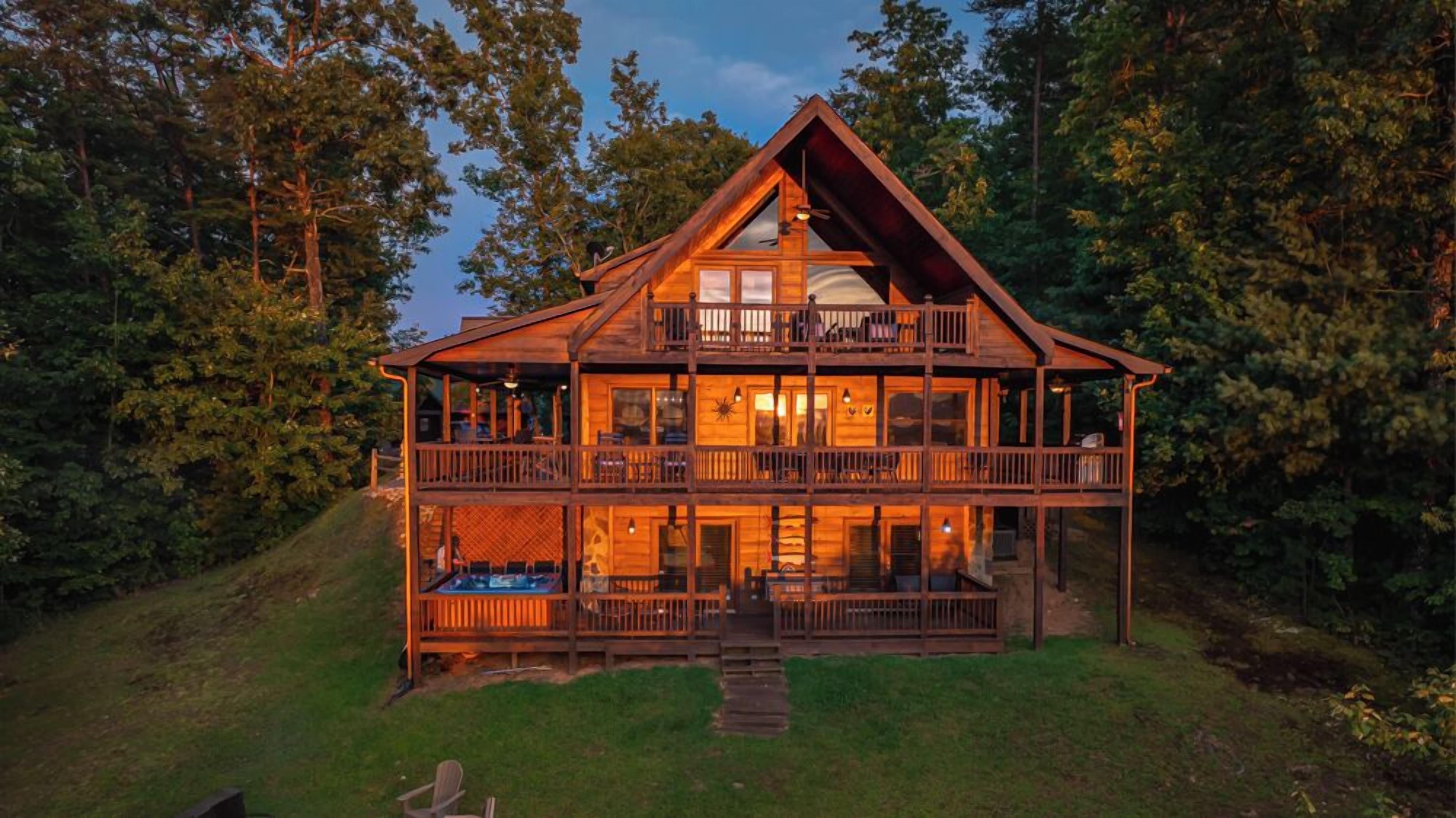 A two-story log cabin with a balcony on the upper floor, surrounded by trees.