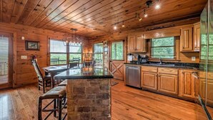 A wooden cabin interior with a kitchen area, a dining table with chairs, and a stone island. - Big Sky Retreat- Pet Friendly | Game Room | Hot Tub with Views (Blue Ridge)
