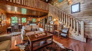 A cozy cabin interior with a wooden staircase, a living area with a sofa and coffee table, and a kitchen with wooden cabinets. - Big Sky Retreat- Pet Friendly | Game Room | Hot Tub with Views (Blue Ridge)