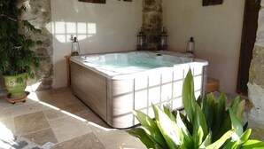 Un espace spa comprenant un jacuzzi, des murs en pierre, des volets en bois et des plantes en pot.