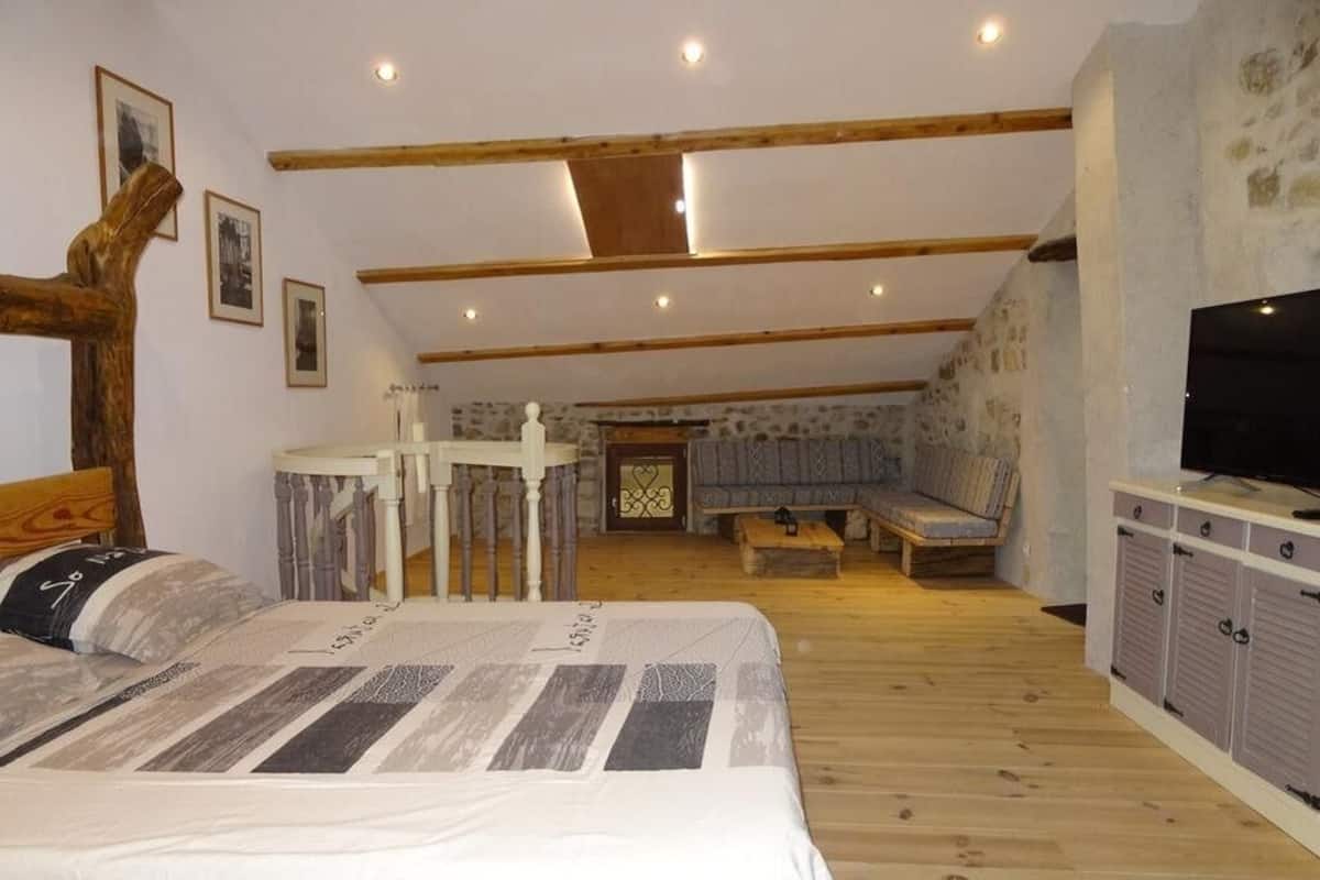 Een slaapkamer met een bed, houten balken, een televisie en een klein tafeltje.