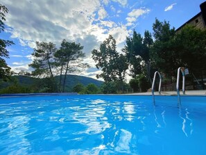 Una piscina con acqua cristallina, circondata da alberi e un edificio.