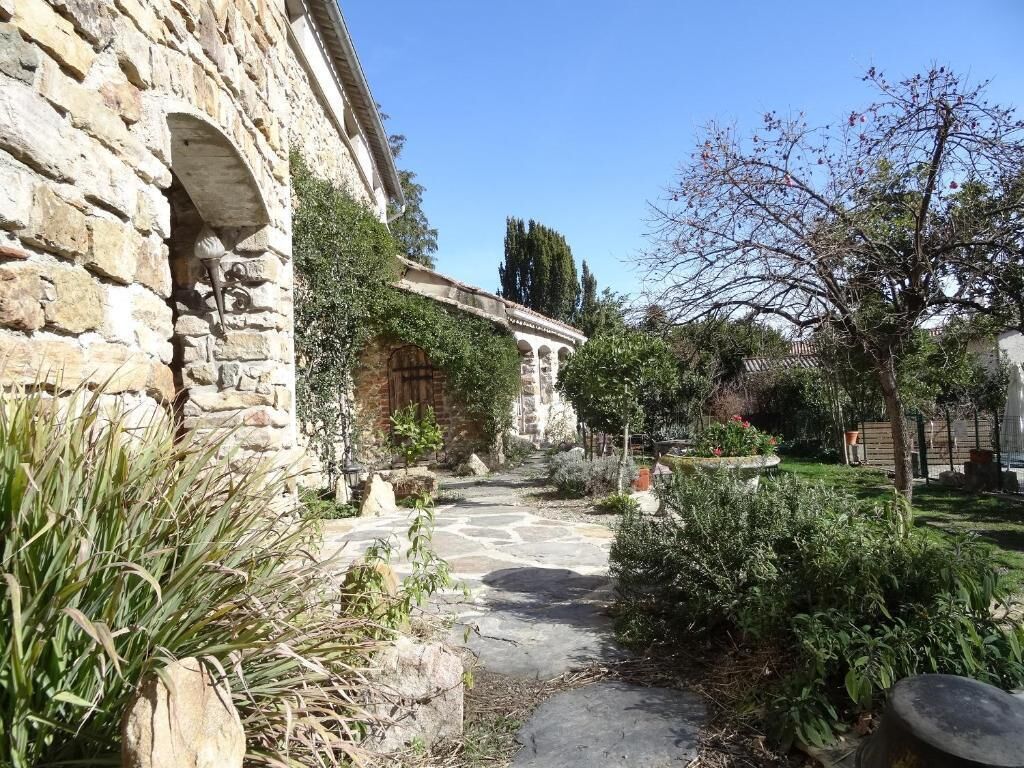 Edificio de piedra con un camino de piedra que conduce a un jardín con diversas plantas y un árbol.