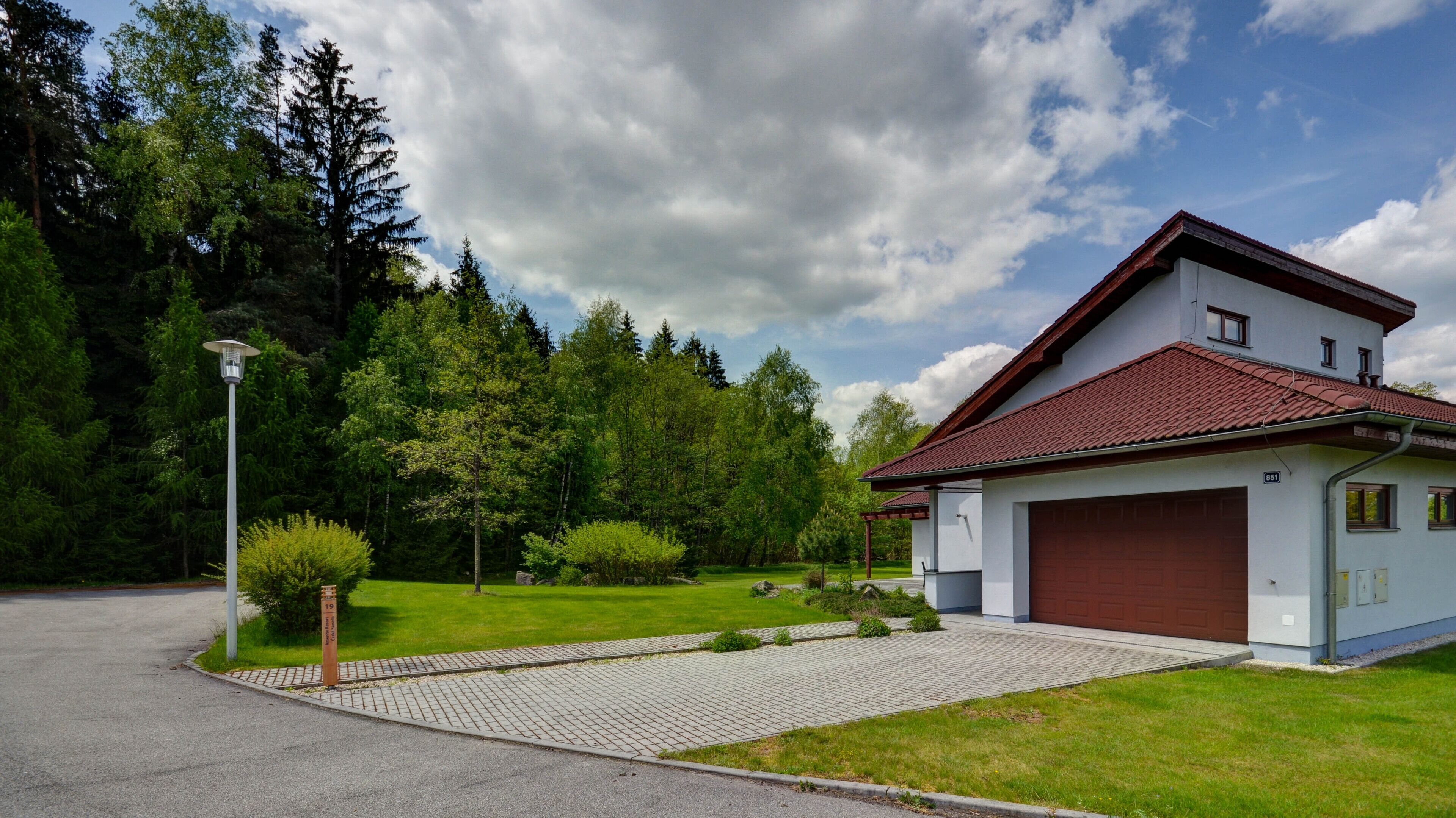 A two-story house with a red-tiled roof, a garage, and a paved driveway leading to the entrance.