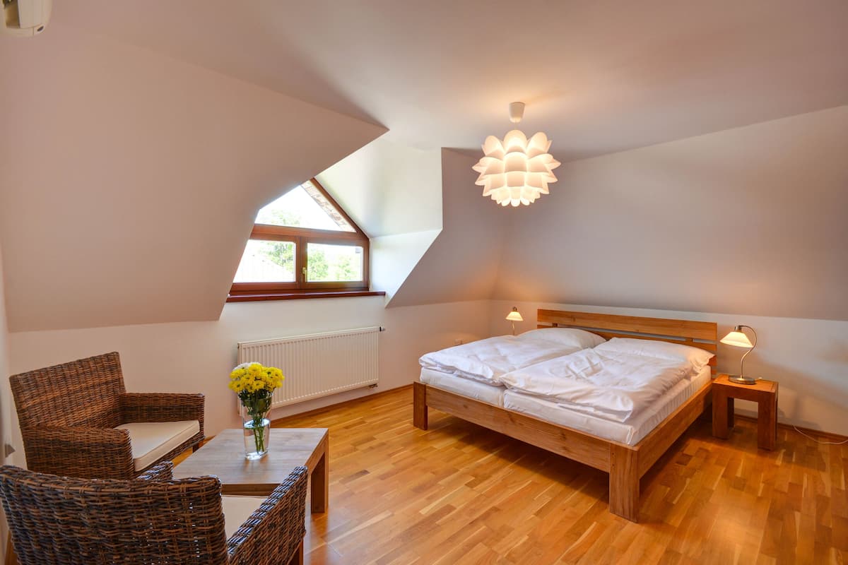 A bedroom with a wooden bed, a small table with a vase of flowers, wicker chairs, and a skylight.