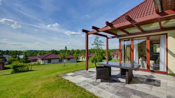 A patio with a table and chairs, a covered area with glass doors, and a view of neighboring houses.