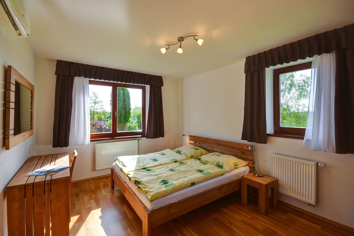 A bedroom with a wooden bed, a desk, and two windows with curtains.