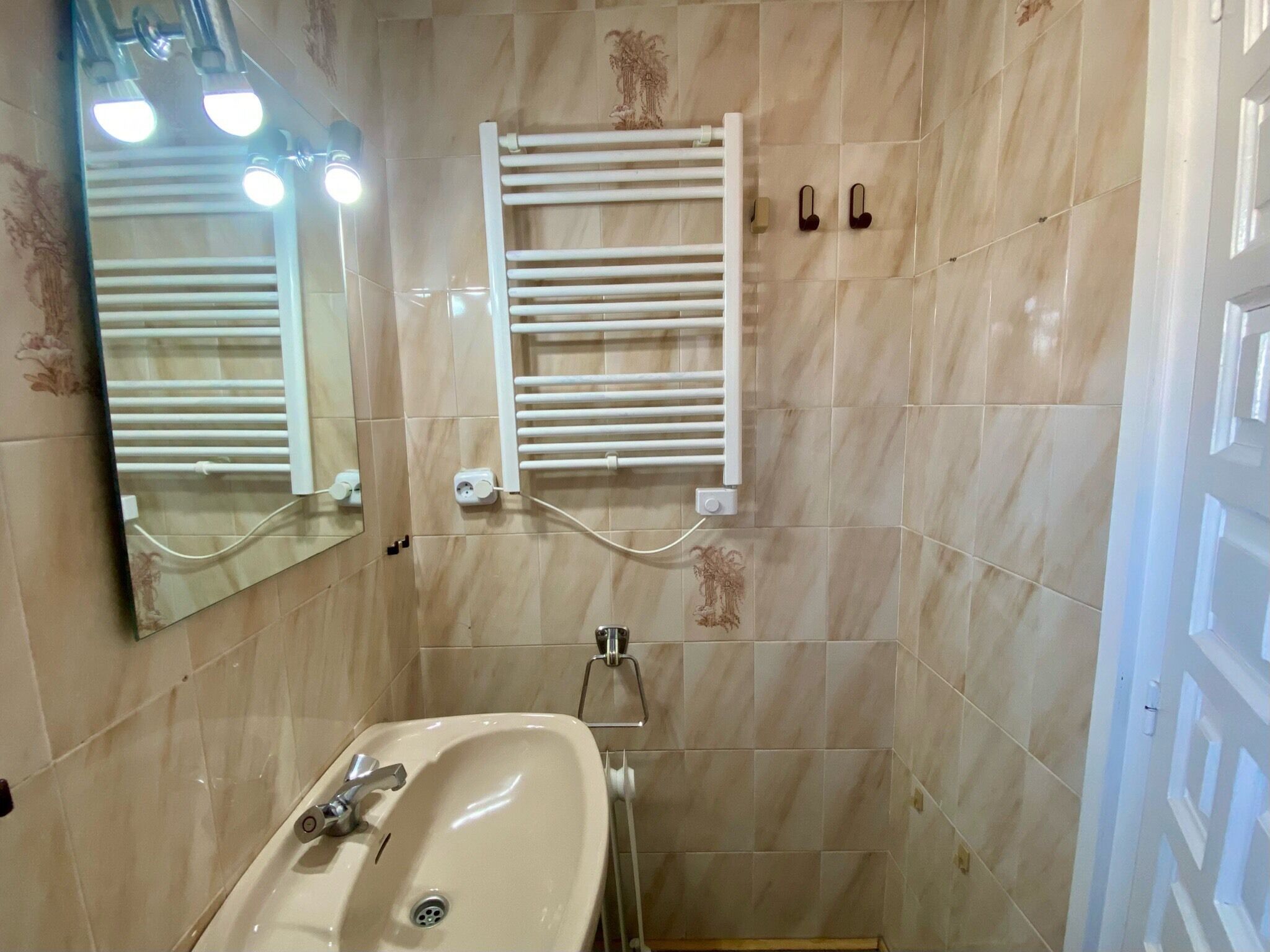 Une salle de bain avec un lavabo, un miroir, un porte-serviettes et des murs carrelés.