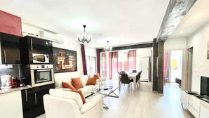 Een moderne woonkamer met een bank, salontafel en een eethoek. Er is een keuken met een magnetron en oven.