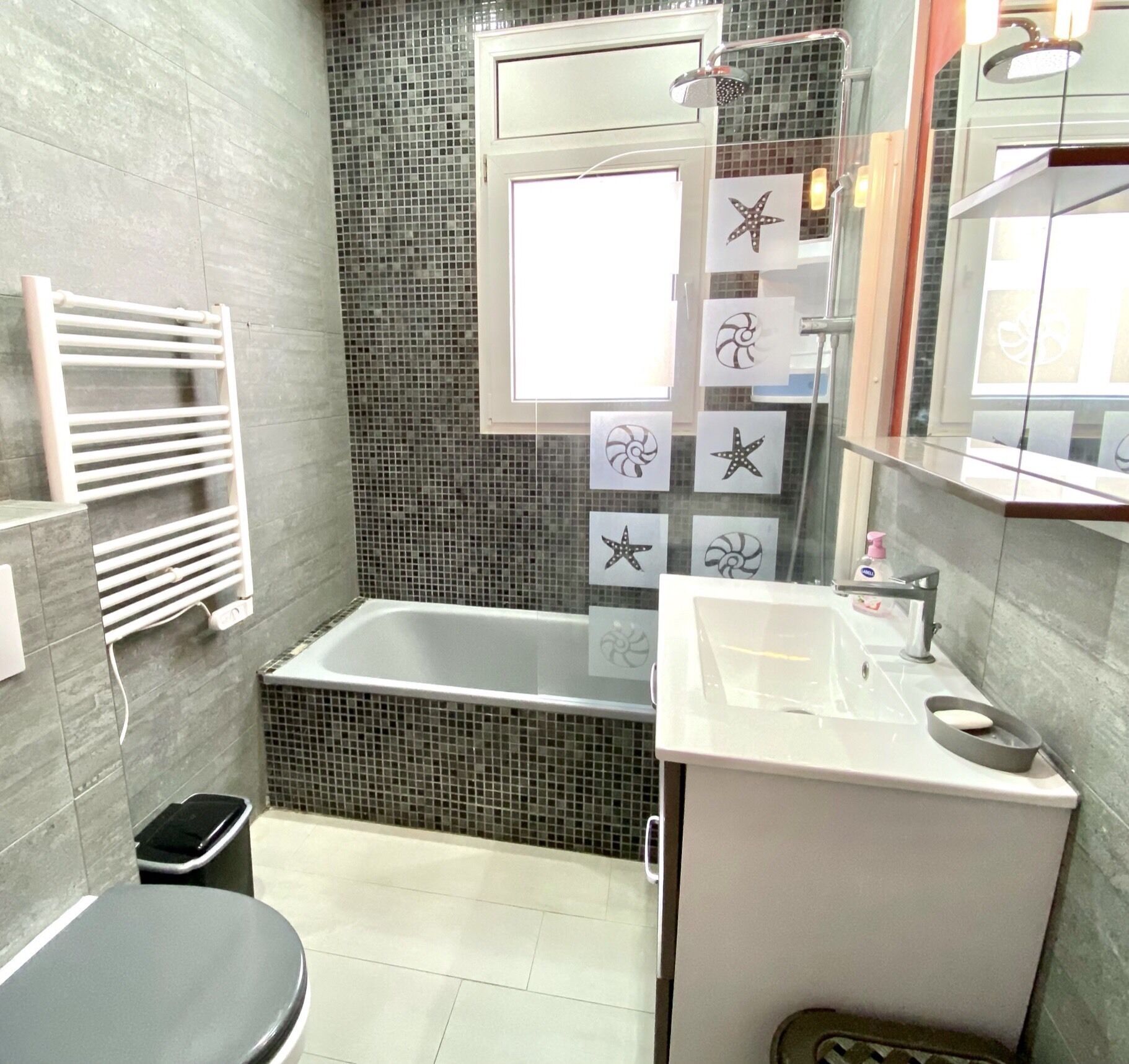 Ein Badezimmer mit Badewanne, Waschbecken und Toilette. Ein Handtuchhalter und ein Mülleimer sind vorhanden.