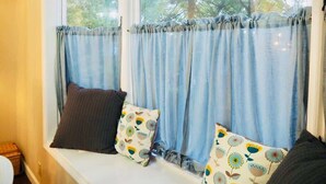 Una habitación con asiento junto a la ventana, cortinas azules y cojines estampados.