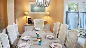 Un comedor con una mesa redonda, sillas blancas, una araña y dos lámparas.