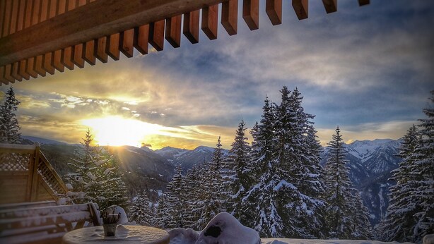 Une pergola en bois offrant une vue sur des montagnes enneigées et un coucher de soleil.
