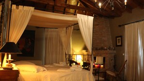 Una habitación con una cama con dosel, un sillón, una mesa con lámpara y una chimenea.