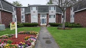 A two-story brick building with a central entrance, a pathway leading to the entrance, and a sign indicating a place for office services.