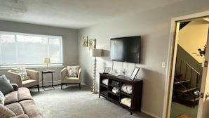 A living room with a sofa, armchairs, a TV, a lamp, and a console table.
