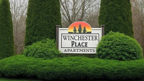 A sign for Winchester Place Apartments with a logo featuring trees and a sunset.