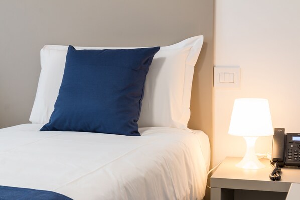 A neatly made bed with white and blue pillows, a bedside table with a lamp, and a phone. - Hotel Cascina Fossata & Residence (Turin)