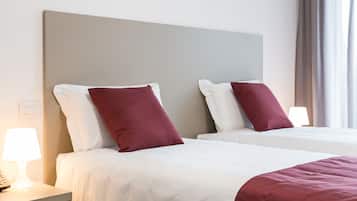 Ein Hotelzimmer mit zwei Betten, weißer Bettwäsche und roten Kissen. Ein Nachttisch mit Lampe und Telefon ist vorhanden.