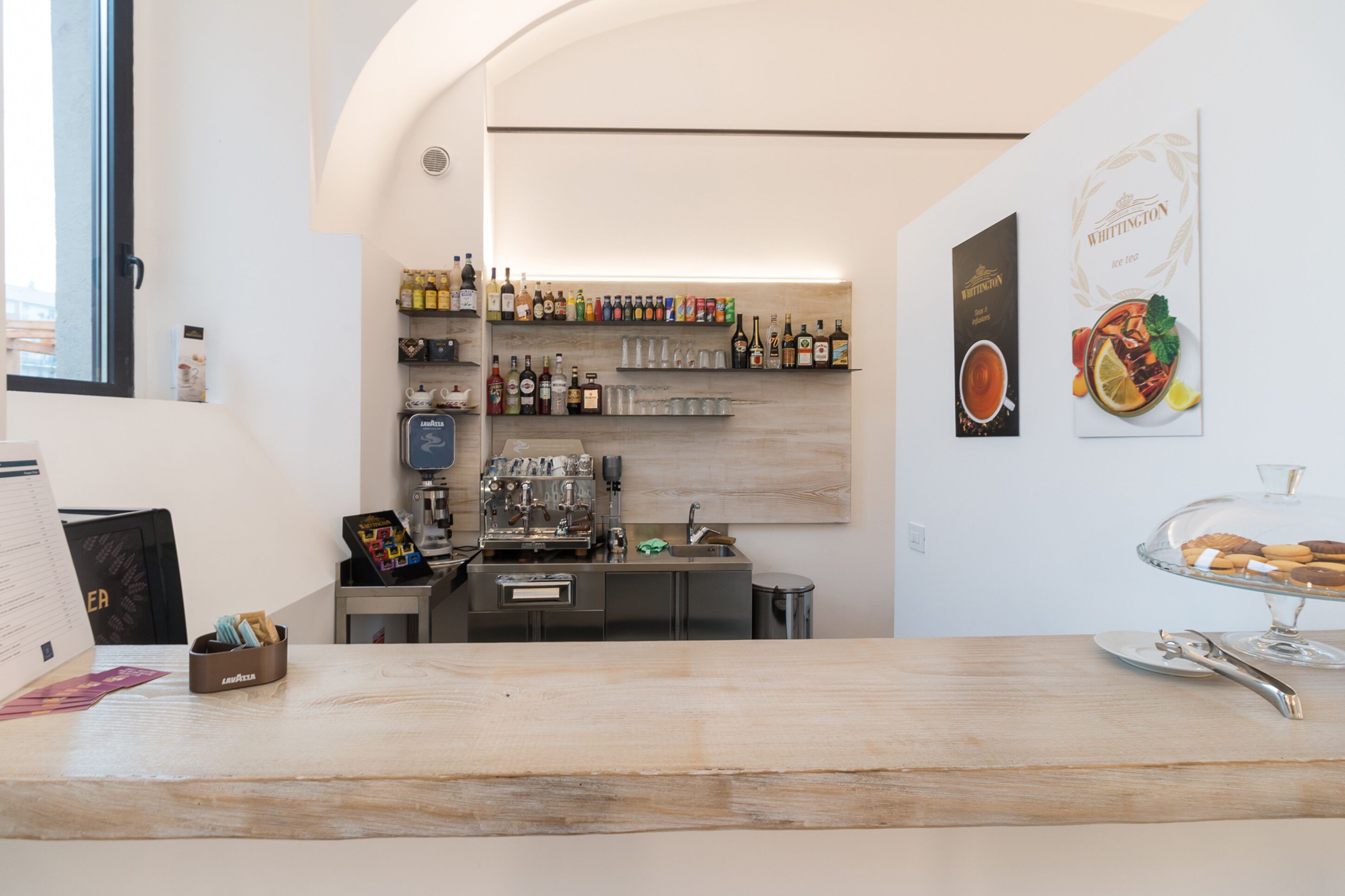 Zona de bar amb un taulell de fusta, prestatges amb diferents ampolles i una màquina de cafè.