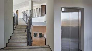 Un interior moderno con una escalera de hormigón, barandillas de metal y un ascensor de acero inoxidable.