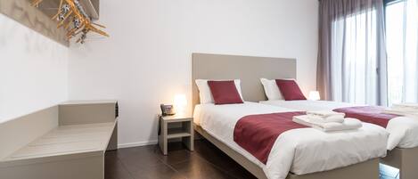 Ein modernes Hotelzimmer mit einem großen Bett, einem Nachttisch mit Lampe, einer integrierten Bank und einem Kleiderschrank mit Kleidung.
