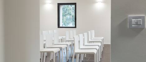 A room with white chairs arranged in rows, a window with a view of trees, and a light switch on the wall.