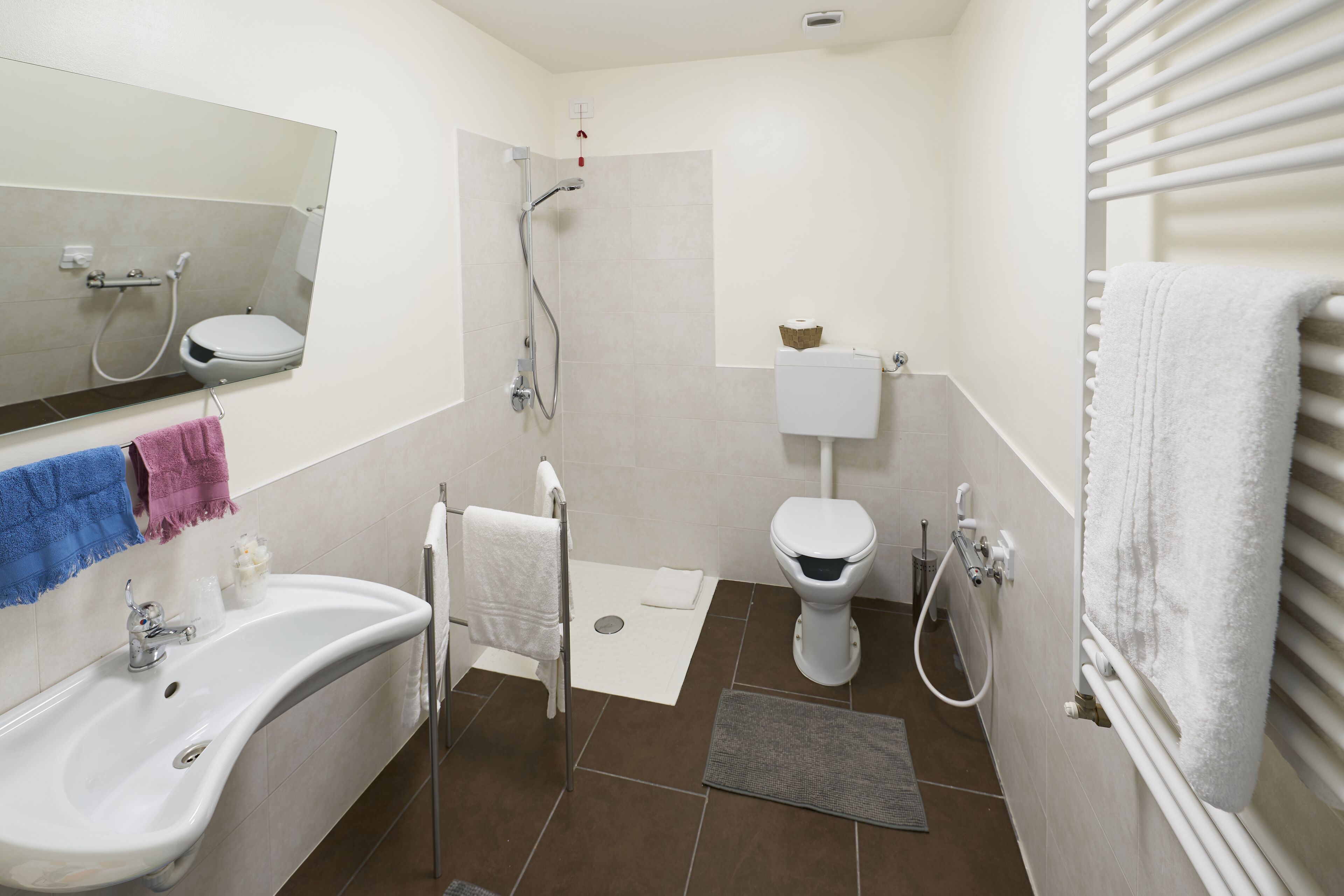 A bathroom with a white sink, toilet, and shower. There are towels hanging on the wall and a mirror above the sink.