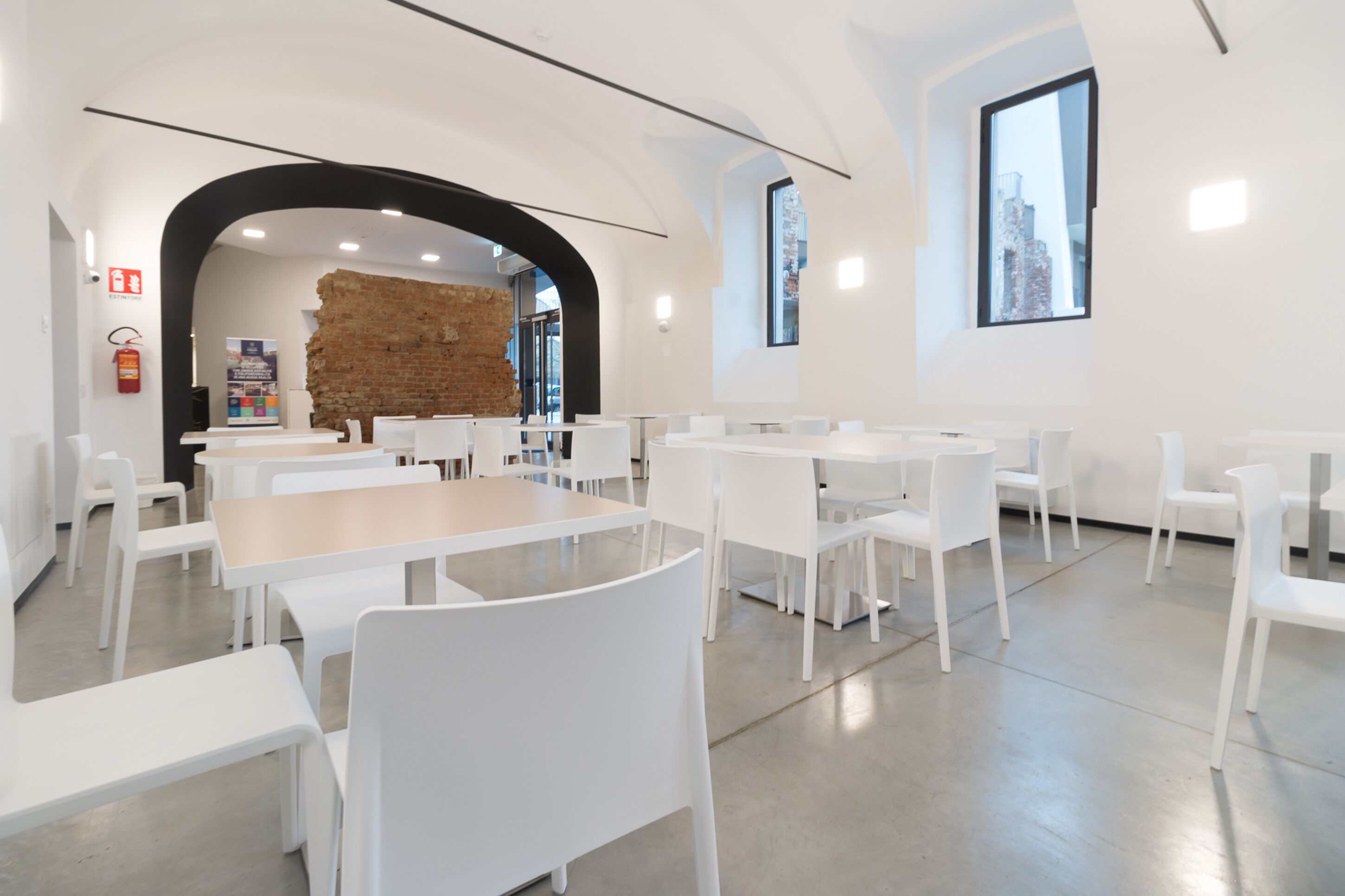 A modern dining area with white tables and chairs, a brick wall, and a large window.