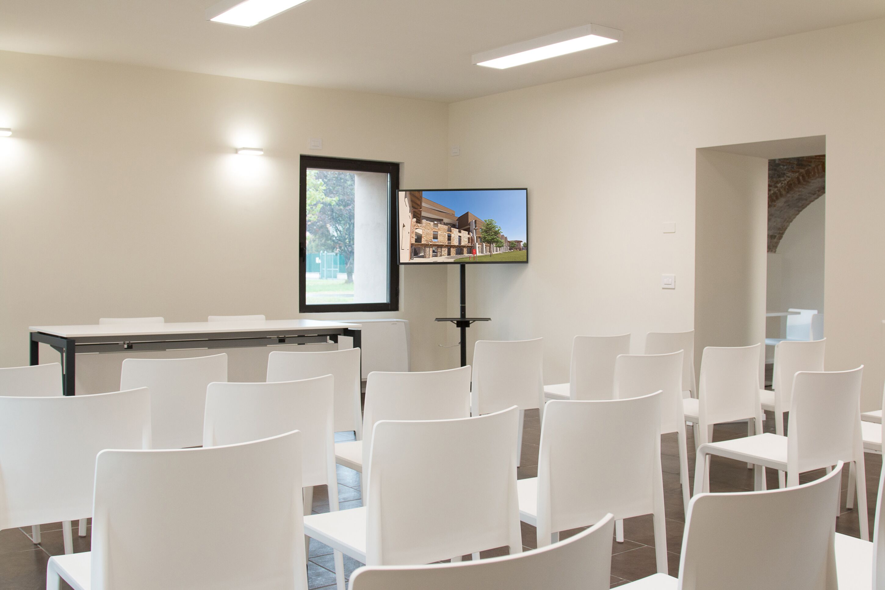 A conference room with white chairs and a table, a framed picture on the wall, and a television screen displaying an image.