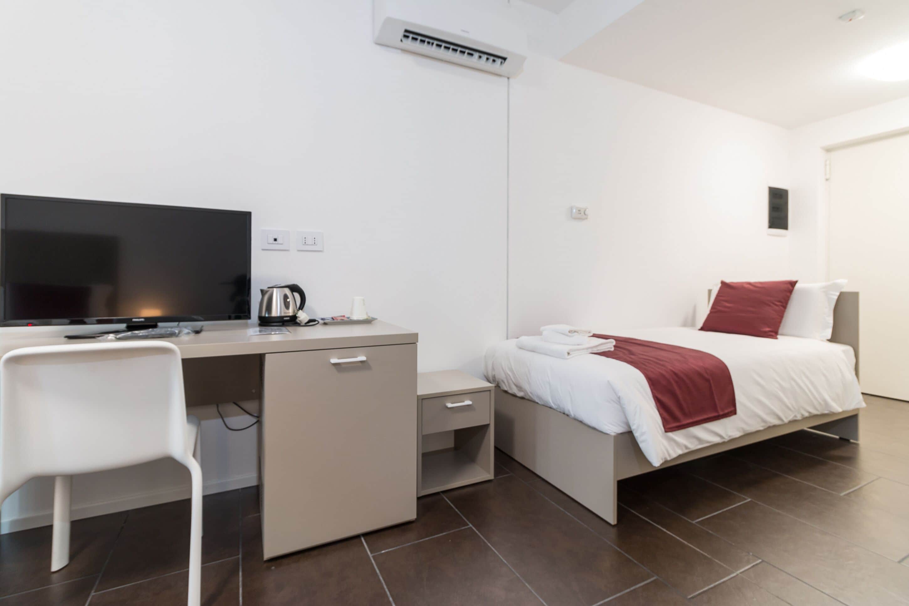 Een moderne hotelkamer met een bed, bureau, stoel, televisie en een kleine kitchenette.