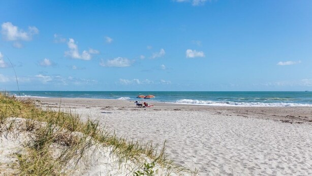 Ein Strand mit blauem Himmel, einigen Personen und einem bunten Sonnenschirm.