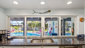 Una cucina con un'ampia finestra vista piscina, una macchina da caffè e uno scolapiatti.