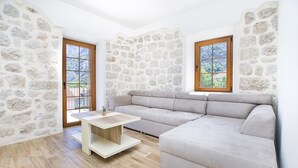 A modern living room with a stone wall, a beige sectional sofa, and a wooden coffee table. - Apartments Mezini 11 (Kotor)