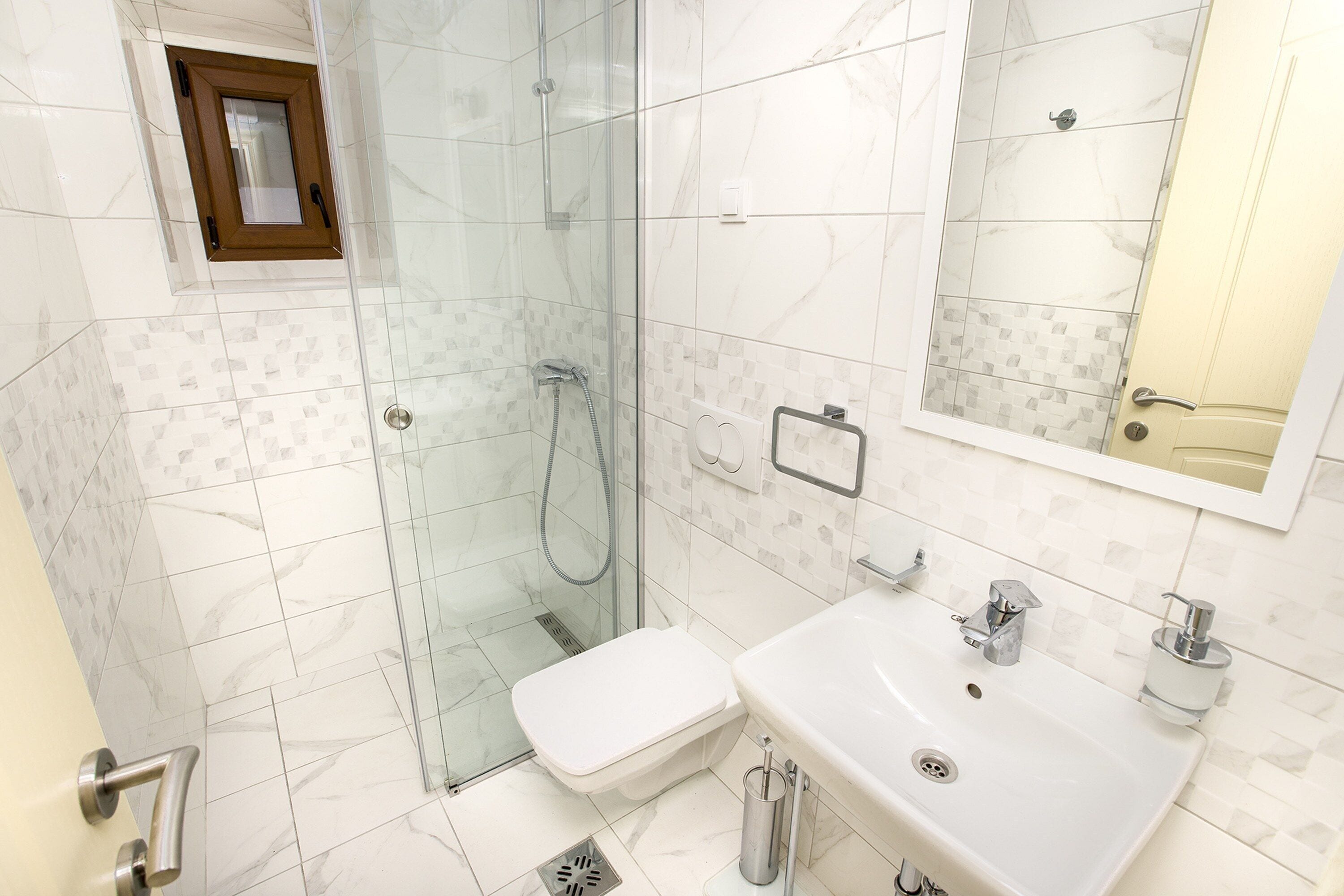 Een moderne badkamer met een douchecabine van glas, een witte wastafel en een toilet.