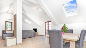 A spacious living area with a high ceiling, a dining table with chairs, a grey sofa, a TV, and a window with a view of the sky. - Apartments Mezini 11 (Kotor)