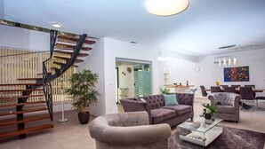 A modern living room with a staircase, a sofa set, a dining area, and a large painting on the wall.