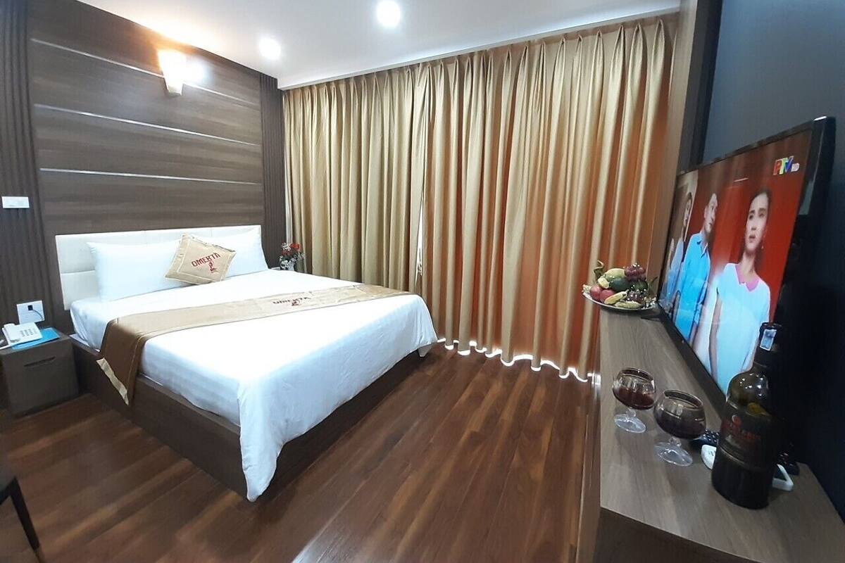 Hotellihuone, jossa on suuri sänky, televisio, yöpöytä ja puulattia.
