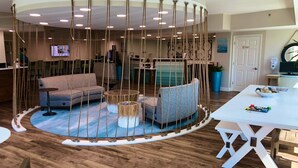 Un espace de détente circulaire comprenant un canapé et des fauteuils, une petite table et une balançoire suspendue.