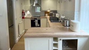 Una cocina moderna con armarios blancos, horno empotrado, refrigerador de acero inoxidable y encimera de madera.