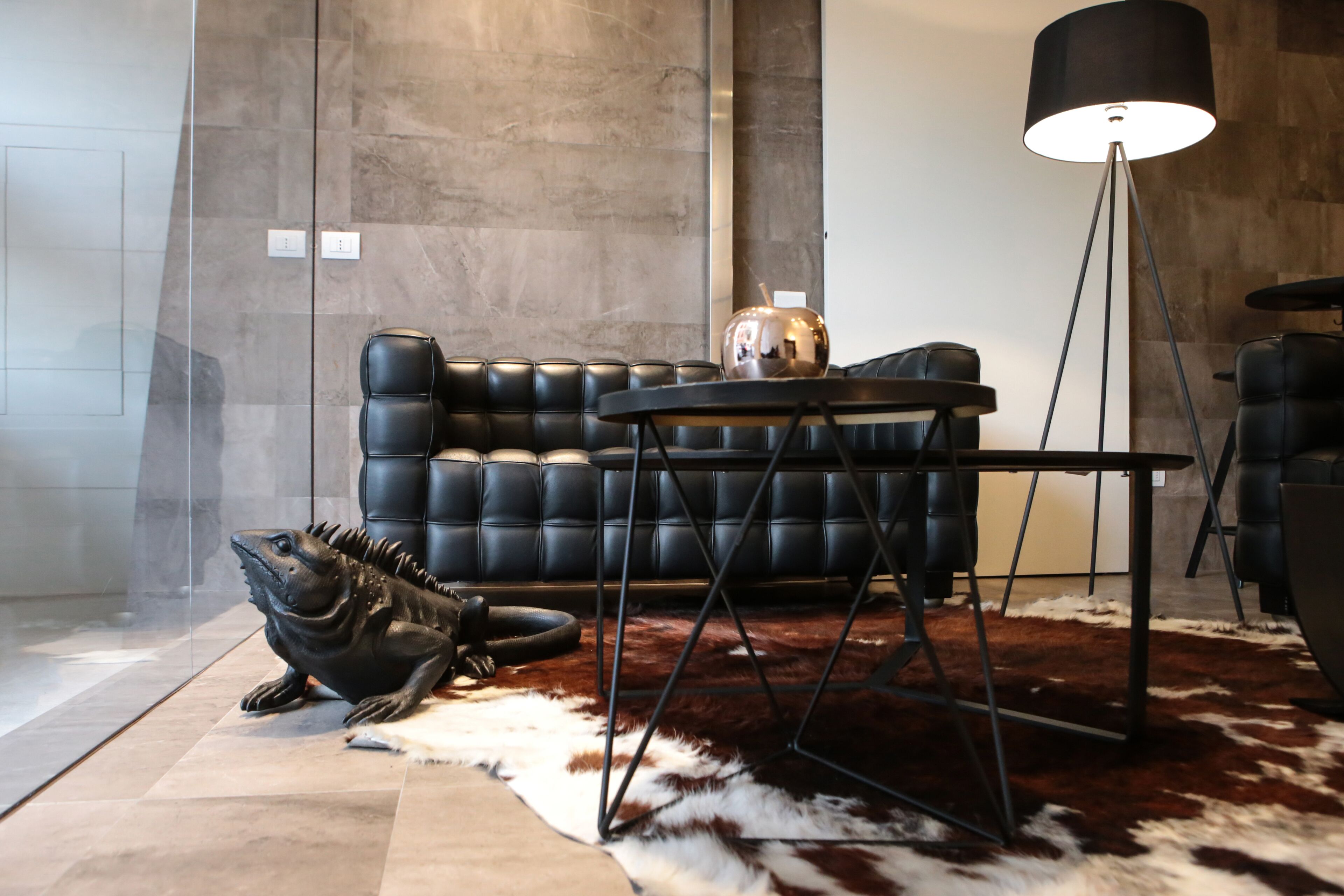 En moderne stue med en lædersofa, et sofabord, en gulvlampe og en stor fiskeskulptur på gulvet.