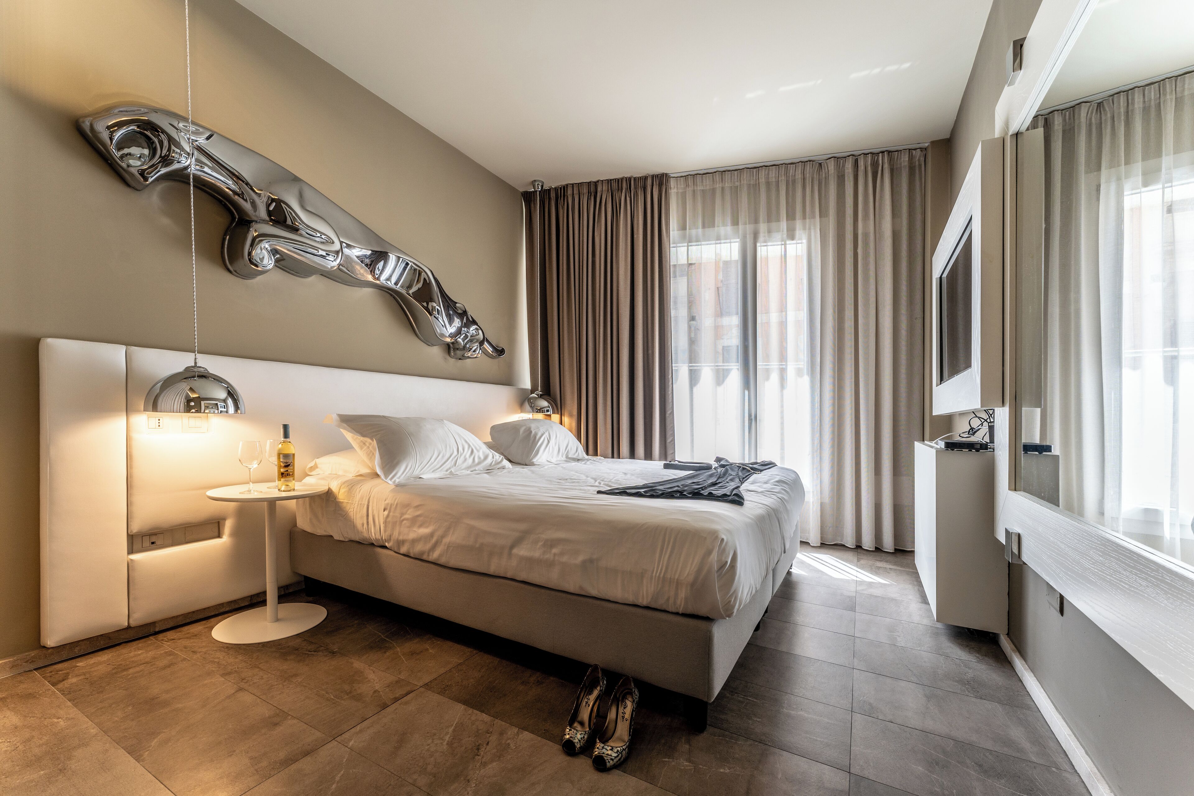 A modern bedroom with a large bed, a side table, a mirror, and a decorative wall piece.