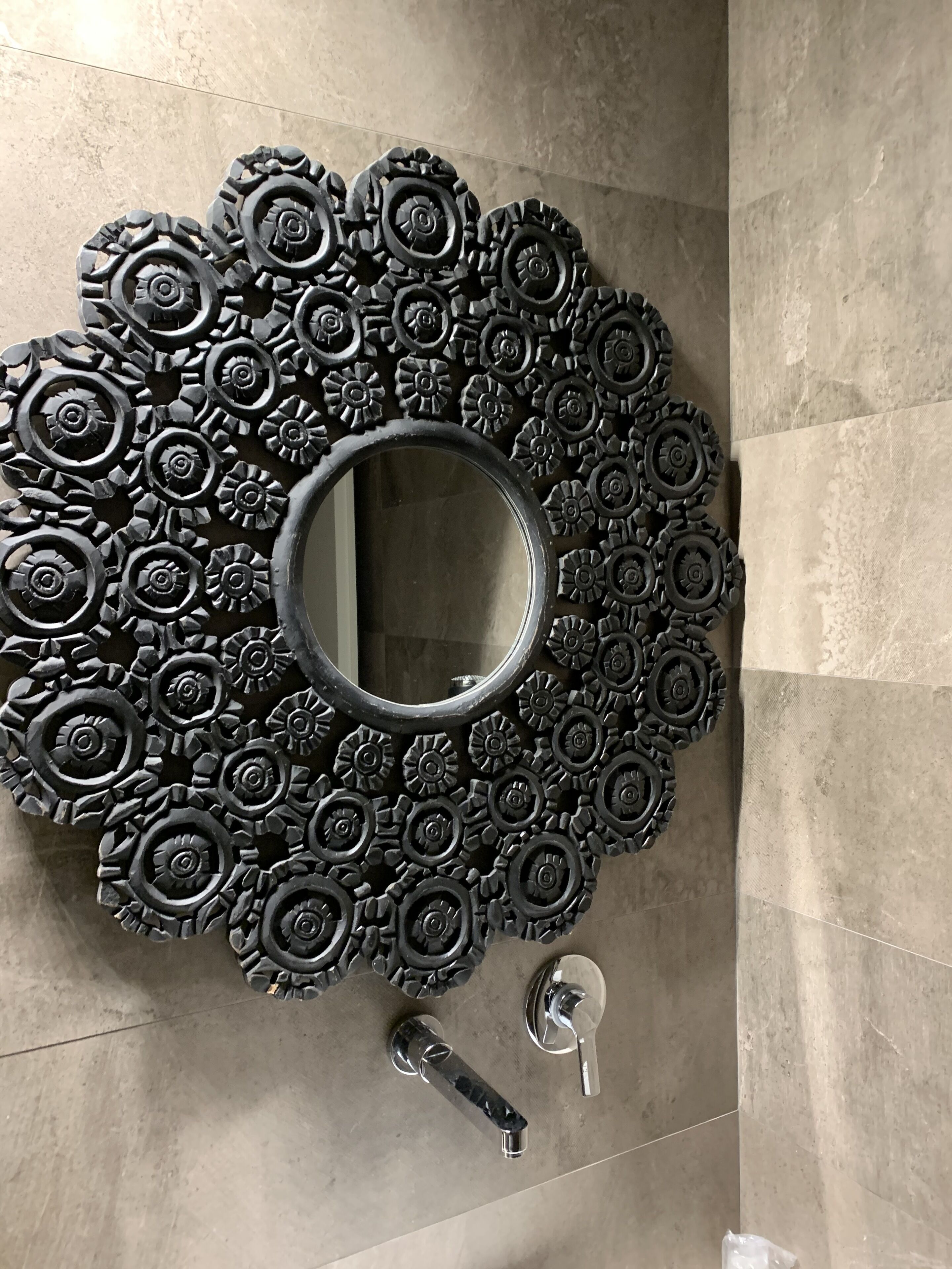 A bathroom with a circular mirror surrounded by a decorative arrangement of black, gear-like objects.