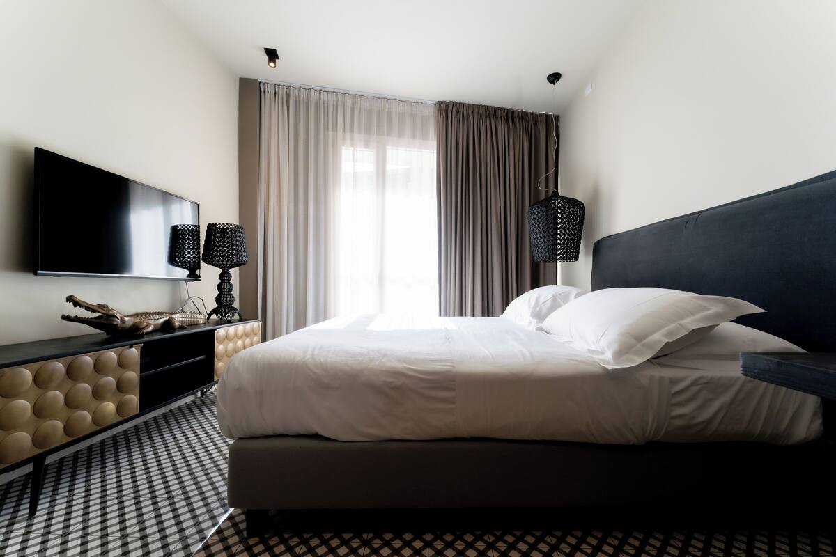 A modern hotel room with a large bed, a flat-screen TV mounted on the wall, a console table with decorative items, and a patterned floor.
