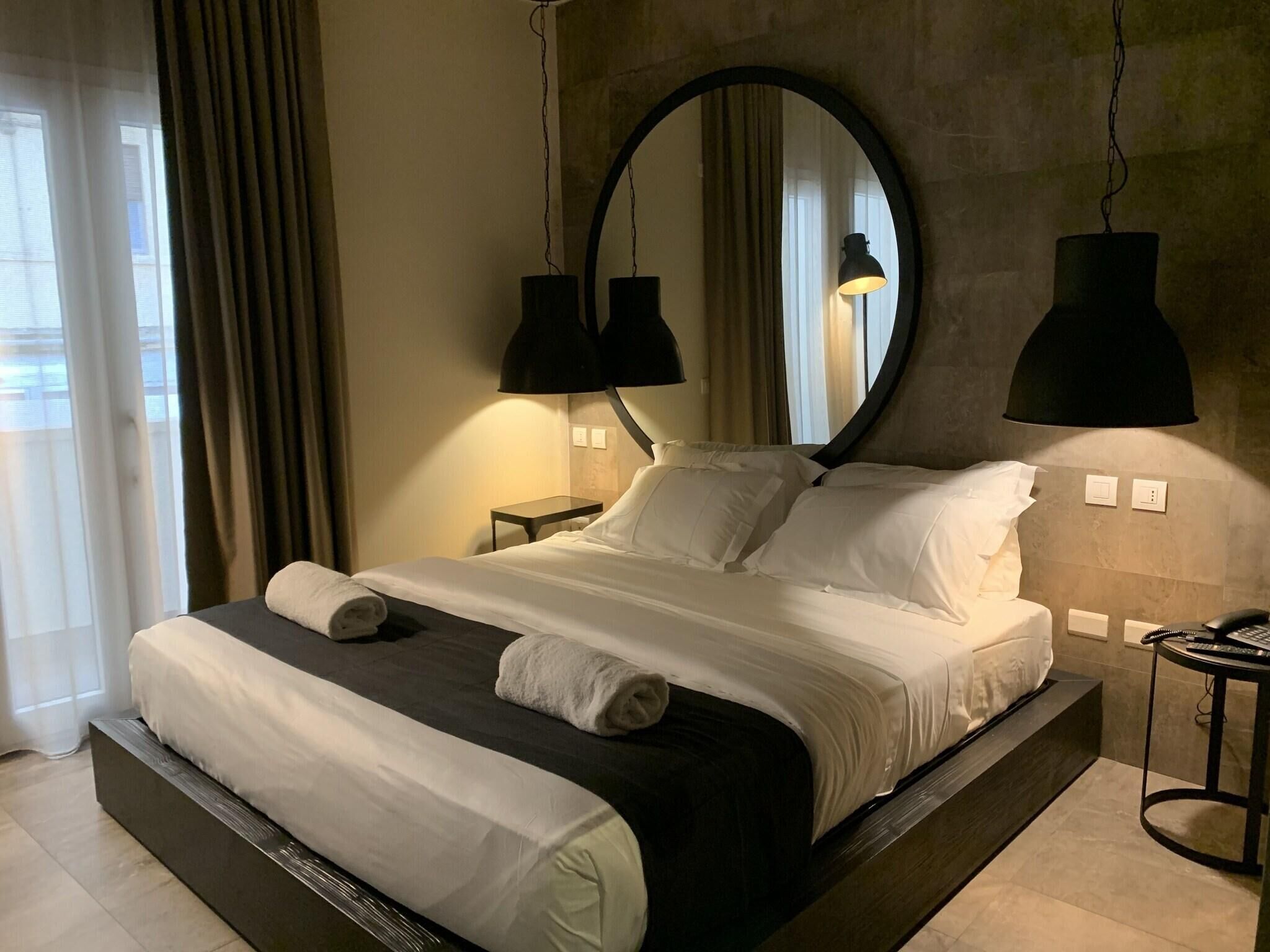 Een moderne hotelkamer met een groot bed, twee bedlampen, een ronde spiegel en een telefoon op een bijzettafeltje.