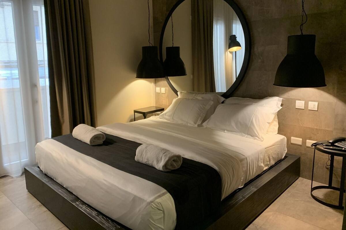A modern hotel room with a large bed, two bedside lamps, a round mirror, and a telephone on a side table.
