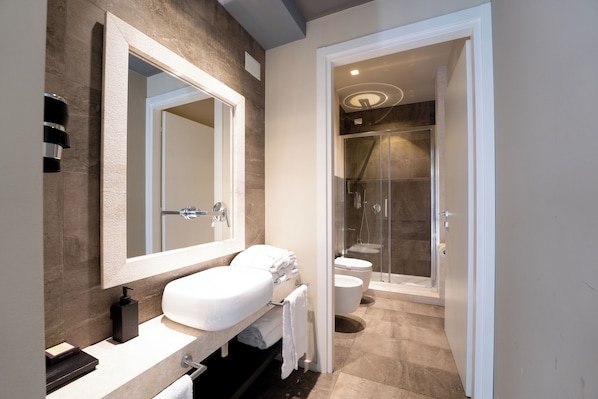 A modern bathroom with a large mirror, a white sink, and a glass-enclosed shower area.