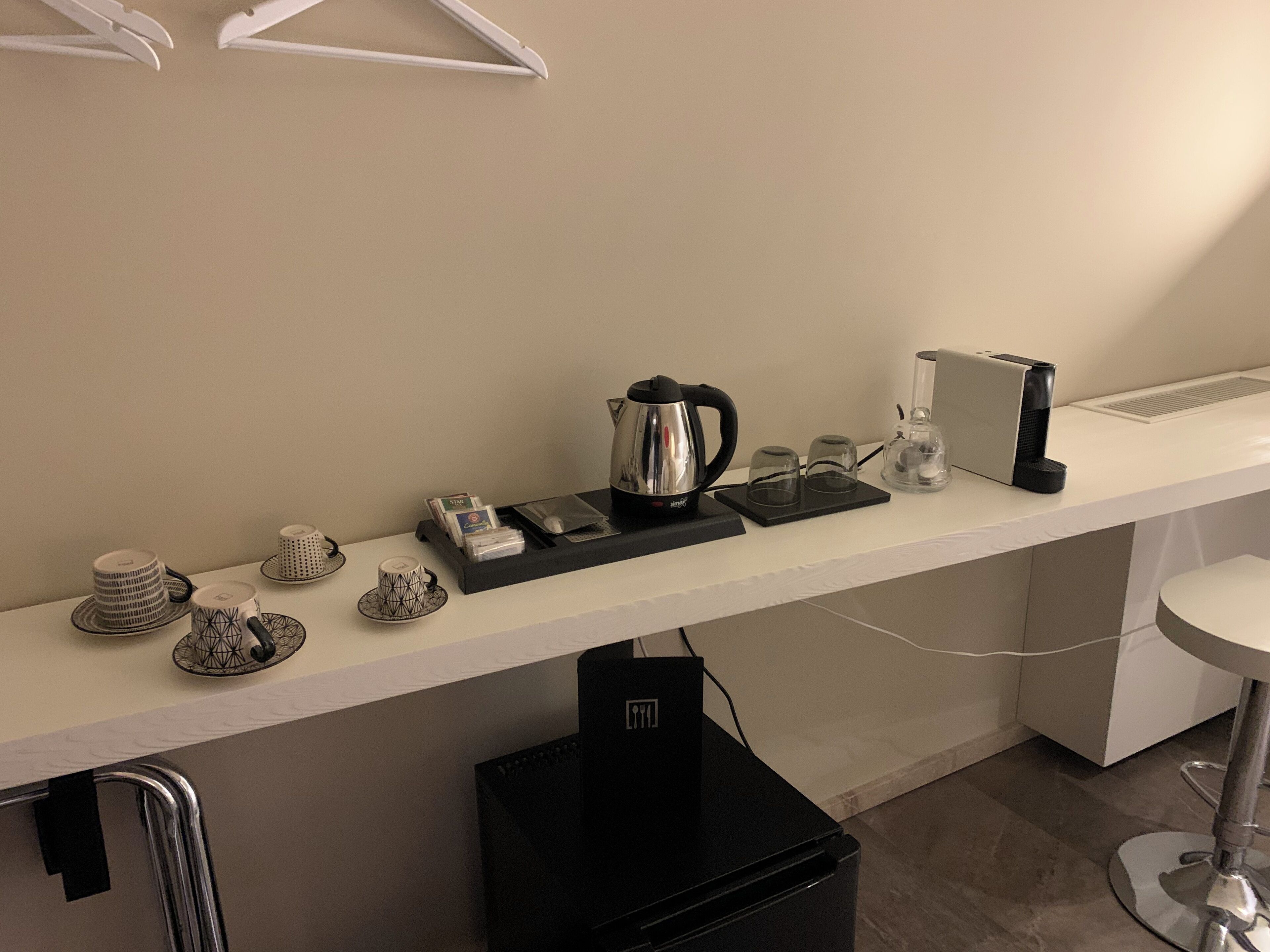 Quarto de hotel com uma bancada comprida, chaleira, cafeteira e um pequeno frigorífico.